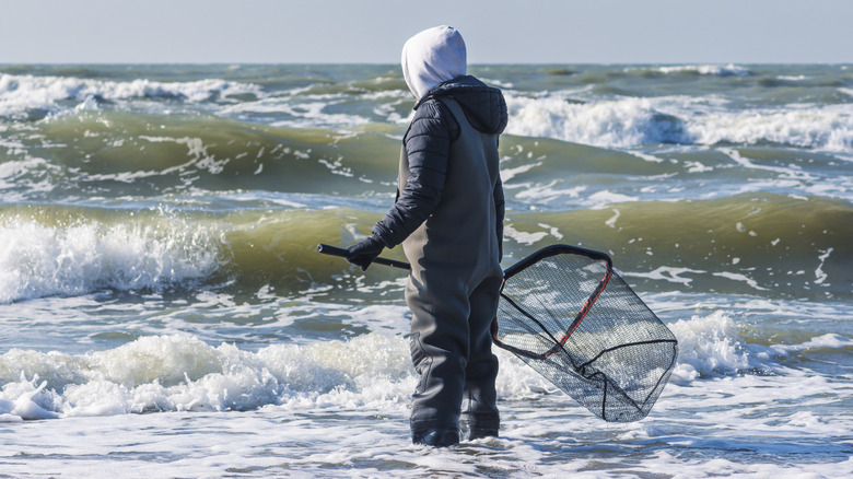 Man wearing fisherman's coat and boots hunting for amber amongst the waves of Lithuania's coast