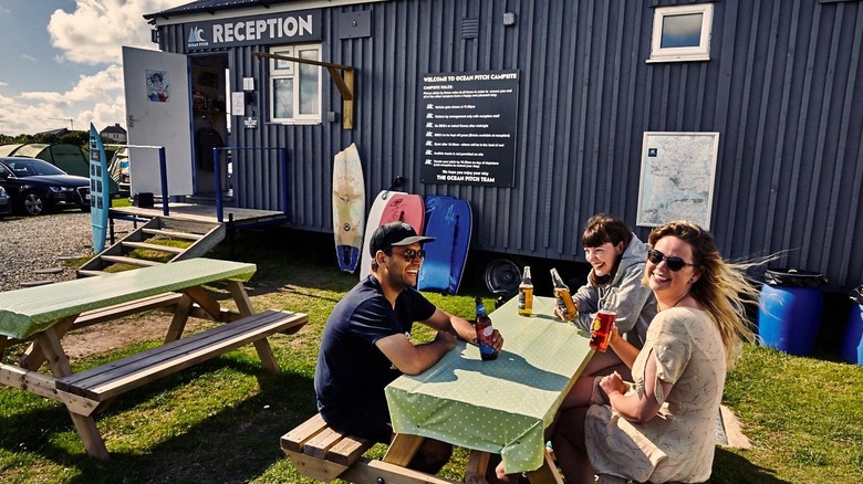 Friends sitting at a table outside the reception hut at Ocean Pitch Campsite Devon, England