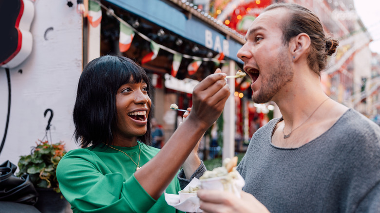 Two people feeding each other food samples.