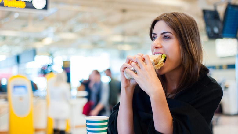 A woman biting into a sandwich in the food court at an airport
