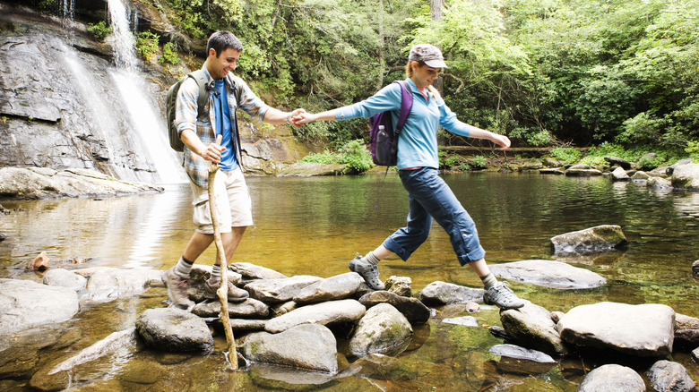 Couple stepping over rocks by waterfall