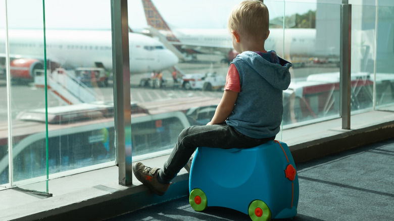 kid riding on his suitcase looking out airport window