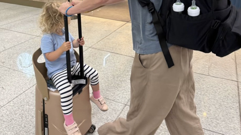 little kid sits atop the MiaMilly suitcase while getting pushed through the airport