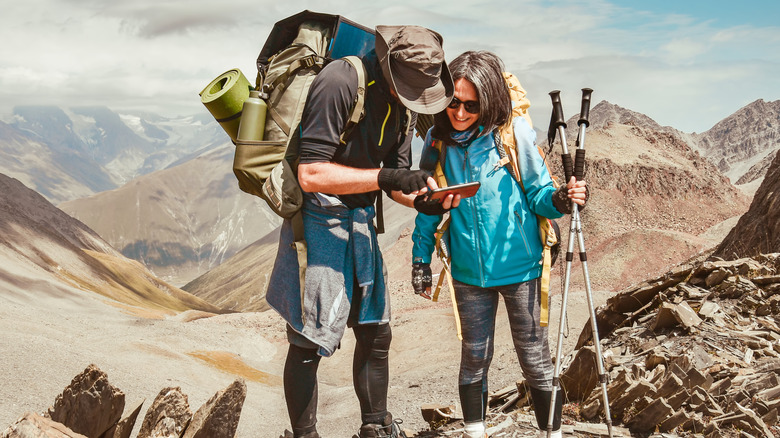 Two hikers use a device while in the mountains