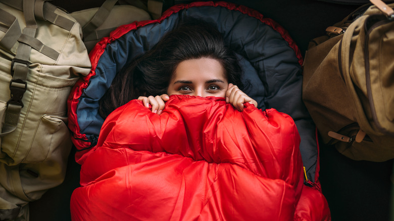 woman peeks her eyes out of underneath a sleeping bag