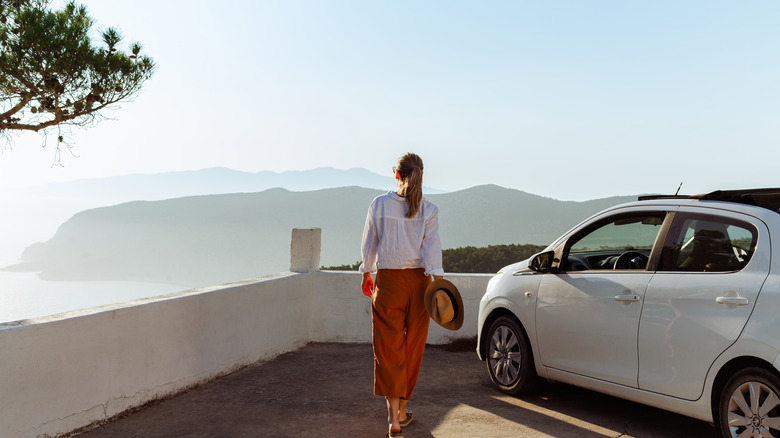 view of woman from behind standing next to white car with mountains in distance