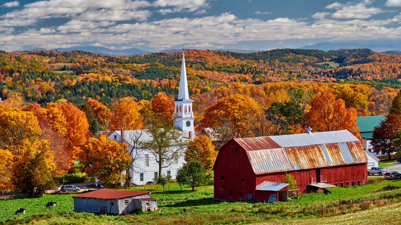 A white church and old red barn during a sunny autumn day surrounded by colorful trees in Peacham, Vermont
