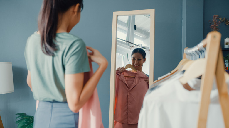 Woman looking in a mirror, holding a dress shirt