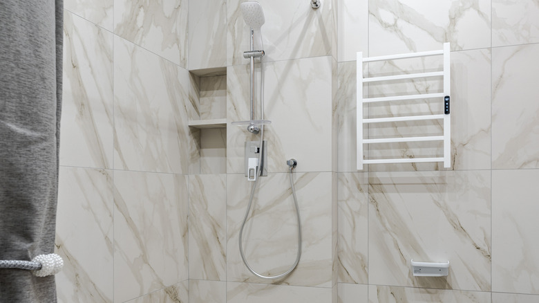 A tiled shower with a shower head and a drying rack