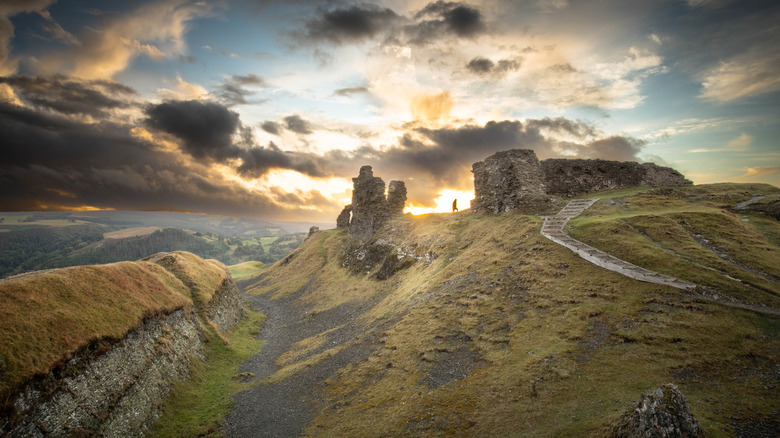 A distant view of a hiker walking through the grey stone ruins of Dinas Bran at sunset.