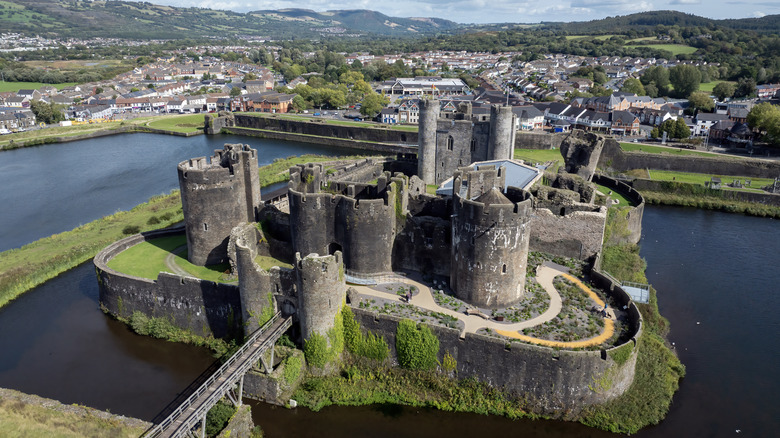 Drone view of Caerphilly Castle, the biggest in Wales, surrounded by a moat with a town in the background.
