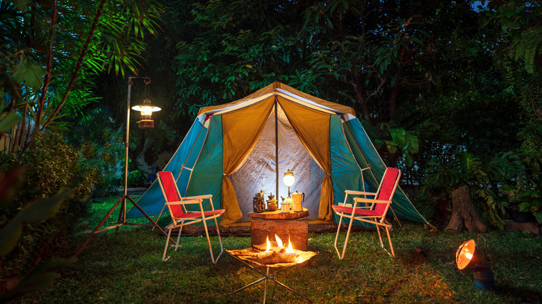 A tent with lanterns behind chairs and a firepit
