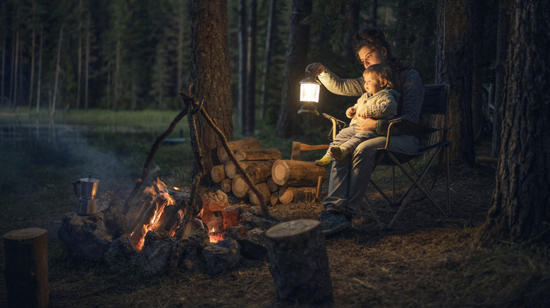 A parent and child with a lantern next to a fire