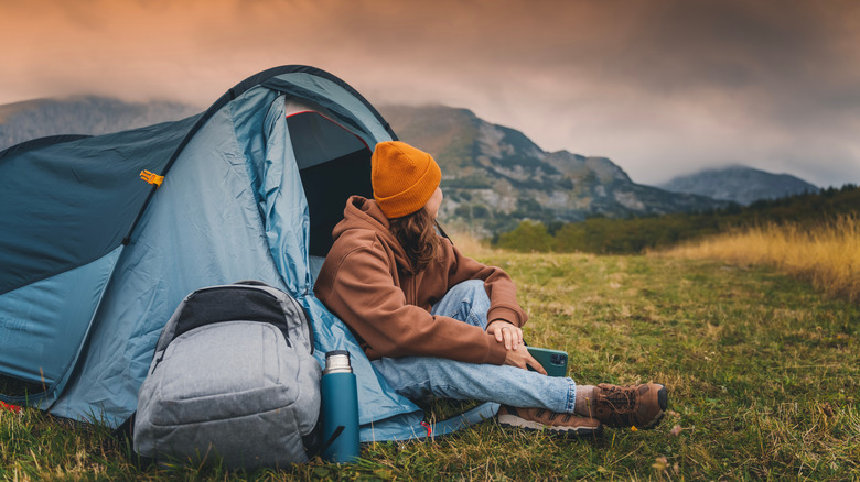 person in tent with backpack looking at mountains