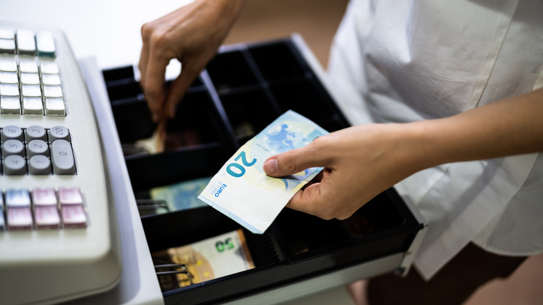 A close-up of a woman's hand taking a 20 Euro bill out of a register