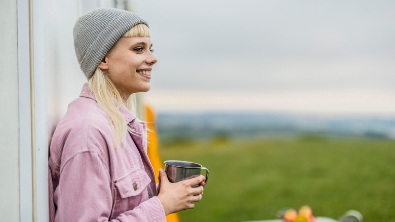 Young woman smiles in a beanie and pink jacket, holding cup
