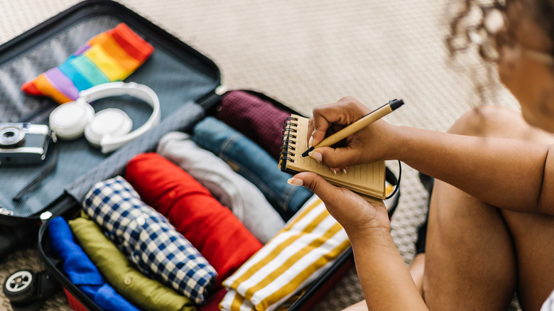 a woman writing after packing clothes and travel accessories in a bag