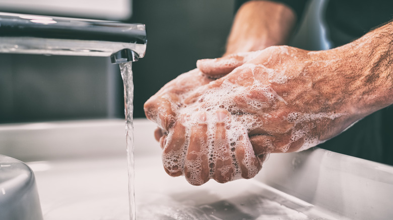 person washing hands at faucet