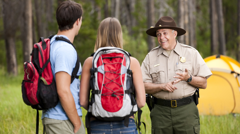 A friendly park ranger stops to talk to two backpackers near their tent in the woods.