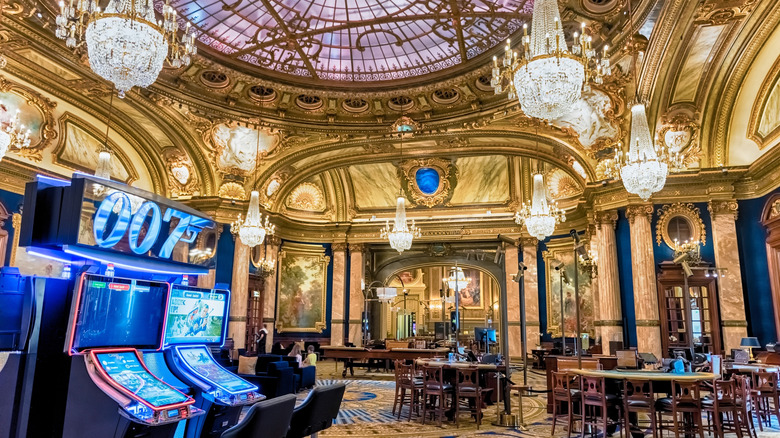 Interior of a casino with large chandeliers, slots and tables with high top chairs