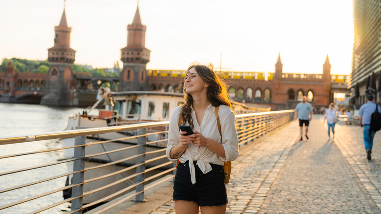 Woman in white shirt using smartphone while walking in Berlin on the background of Oberbaumbrucke