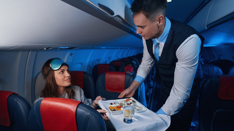A woman with an eye mask looking at a flight attendant while taking her meal.