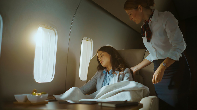 A flight attendant trying to wake a sleeping passenger.