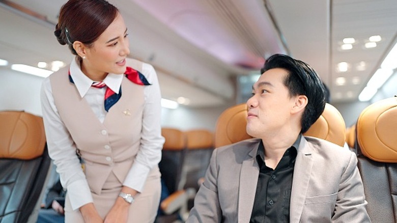 A flight attendant talks with a passenger on an airplane.