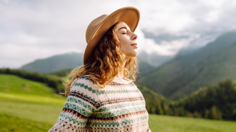 A woman inhales deeply in an alpine meadow.
