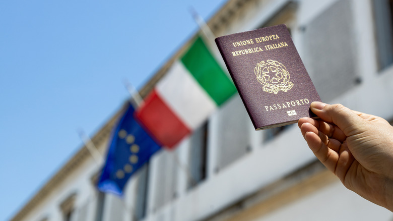 A hand holding an Italian passport and a European Union flag waving in the background