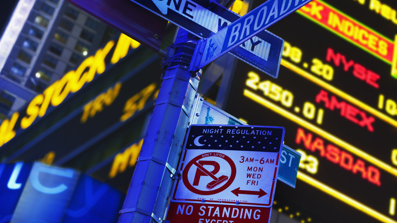 A cluster of confusing street signs hang in front of the stock market ticker in New York City