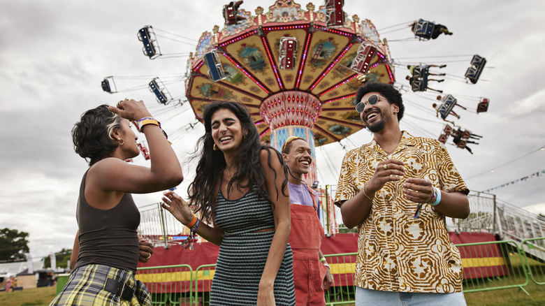 Cheerful multiracial friends standing against chain swing ride at music festival