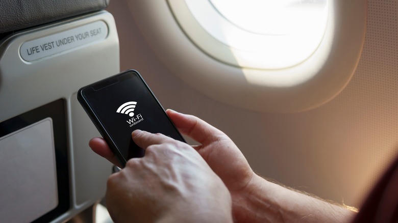 hand holding cell phone showing Wi-Fi logo next to plane window