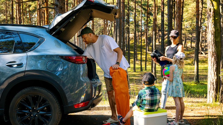 Family with kids getting camping supplies from car trunk