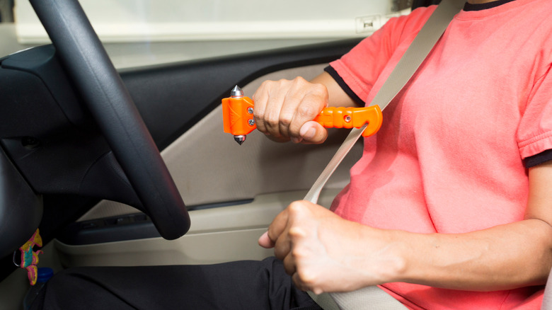 Driver using safety hammer and seatbelt cutter in a car