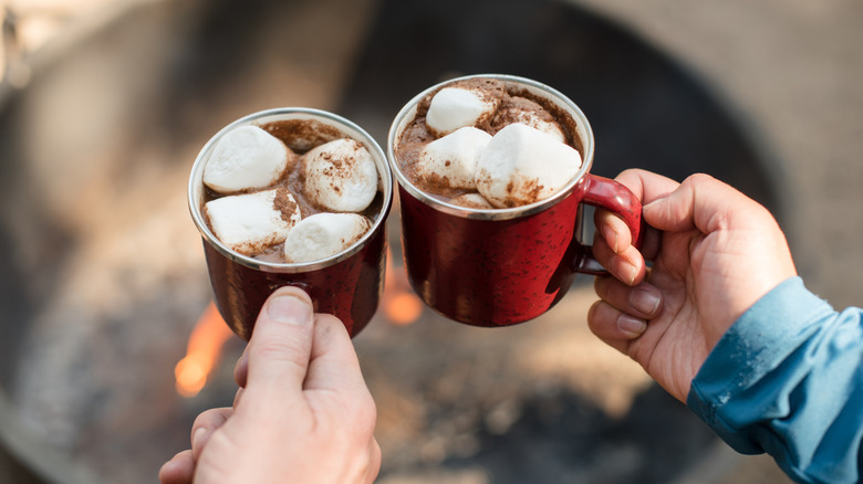 Cups of hot chocolate with marshmallows above a campfire