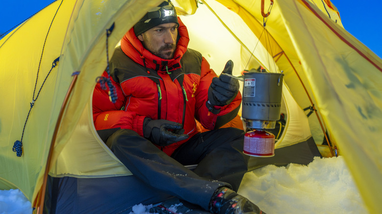 A winter hikers uses a camp stove suspended from his tent frame