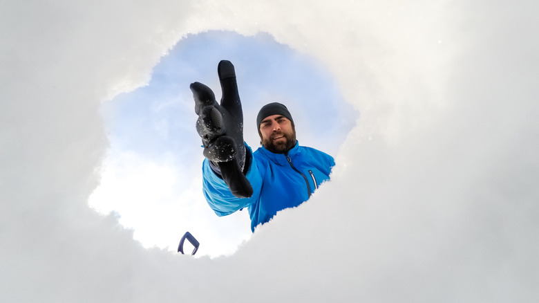 A bearded man extends a hand into a hole dug into the snow