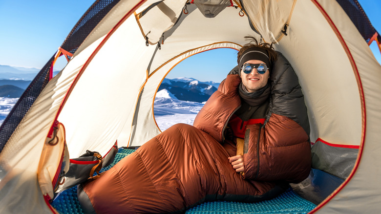 A man in a sleeping bag camping in a snowy landscape.