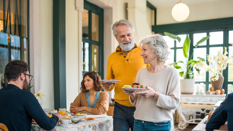 An older couple walking with plates in a small hotel dining room