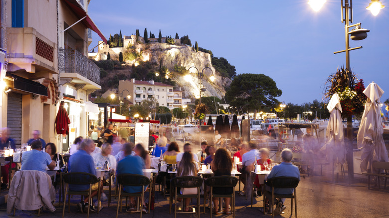 People dining in outdoor restaurant with French scenery in background