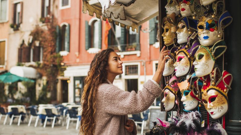 A woman browsing beautiful handmade carnival masks at a street kiosk.