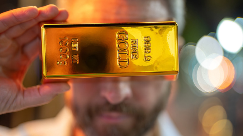 Rich businessman holding a gold bar in front of his face