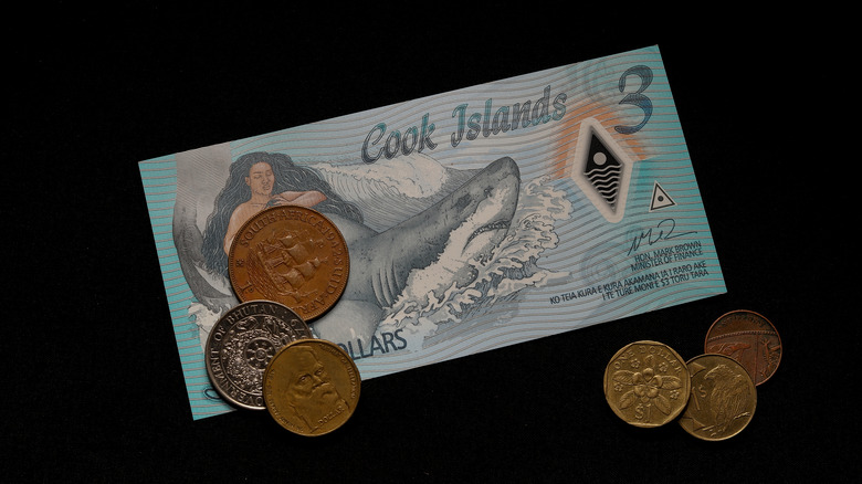 A Cook Island three dollar bill and assorted change on a black background