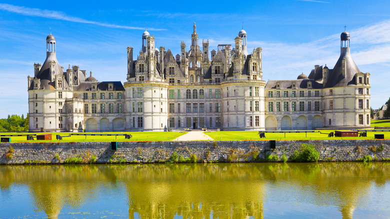 Great panoramic of Chambord Chateau reflected in the canal in a summer day with blue sky.