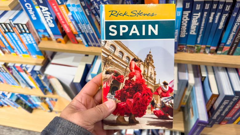 Person pulling "Rick Steves Spain" book from bookshelf