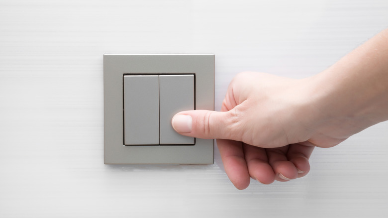 A hand using the thumb to activate a light switch on the wall