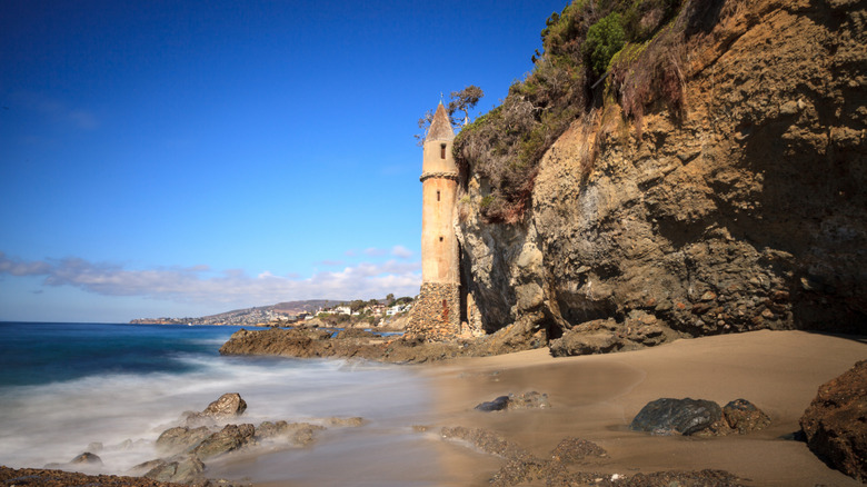 cliff with stone tower, sandy beach, and blue sky