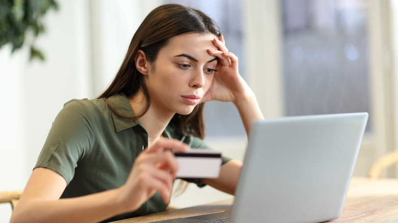 disappointed woman with a credit card looks at a laptop