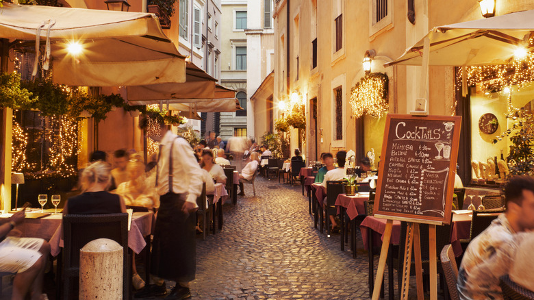 A narrow street of Italian restaurants with a chalk menu board.